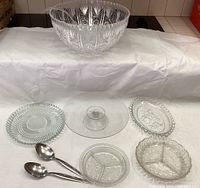 All items in the lot displayed together: large cut and frosted glass bowl, clear glass cake stand, multiple glass trays, and two stainless steel spoons