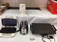 Set of the small kitchen appliances shown on white cloth; waffle maker, toaster, can opener, electric griddle, and Tupperware bowl visible.