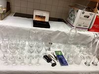 Wide view of all stemware and bar tools arranged on a covered surface including wine glasses, tumblers, decanter, and several bar tools.