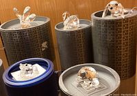 Four figurines displayed on and around cylindrical Swarovski boxes: frog, turtle, swan and octopus visible