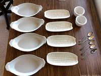 Photo of four white porcelain corn plates with handles, four rectangular corn-themed white dishes and two small white bowls on wooden table