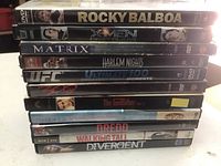 Stack of 10 DVD cases with spines showing titles: Rocky Balboa, X-Men, Matrix, Harlem Nights, UFC Ultimate 100 Moments, 300, The Godfather, House of FX, Dredd, Walking Tall, and Divergent.