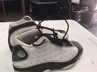 Side view of the Air Jordan Retro 13 shoe showing white with black and green accents, visible dirt and wear.