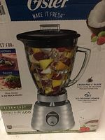 Photo of the Oster blender box showing the blender filled with cut fruit inside the glass jar. The box highlights the Crush Pro 4+ blade and ice crushing power.