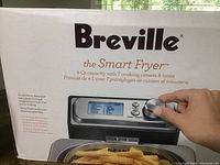 Box of Breville the Smart Fryer showing front panel with digital display and rotary dial being adjusted by a hand.