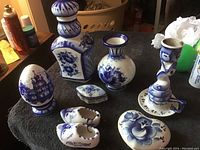 Photo of multiple vintage Russian Gzhel porcelain figurines and objects on a table, showing detailed hand-painted blue floral and traditional motifs on white porcelain.