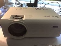 Front and top perspective of the Ematic projector showing lens, brand logo, focus dial, and control buttons.