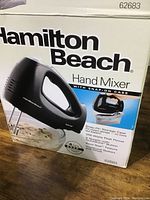 Photo of the box showing Hamilton Beach Hand Mixer branding and features including snap-on case, 250 watts, quick burst button, 4 speeds.