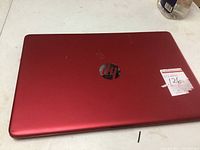 Closed red HP laptop showing top cover with HP logo and condition sticker
