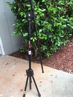 Black Proline adjustable stand with tripod legs, shown outdoors on concrete near greenery.