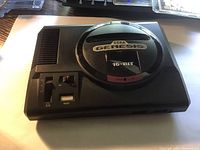 Top view photo of Sega Genesis 16-bit game console showing power switch, reset button, volume slider, and cartridge slot with branded label.