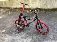 Child's sparkle bike with pink tires and training wheels alongside a red pogo stick with black grips