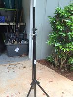 Full view of the black adjustable metal stand in an outdoor environment showing tripod base and height adjustment knobs.