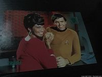 Color photograph showing two Star Trek characters (Nyota Uhura and Captain James T. Kirk) in a scene, part of collectible cards.