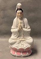 Front view of the white porcelain Guan Yin seated figurine on pink lotus base with detailed facial features and painted patterns on robes.