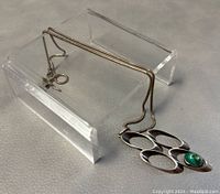 Photo of the necklace laid on a clear stand showing the full chain and pendant with oval cut-out design and green Eilat stone.