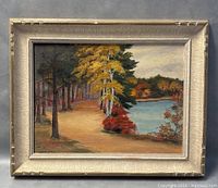Full view of the oil painting showing the autumn landscape with trees and water inside a silver textured frame.