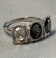 Close-up photo of silver-tone Swarovski ring featuring three oval faceted Austrian crystals, one clear and two black, with beaded silver-tone framing.