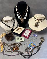 Full view of the assortment of vintage costume jewelry items including various necklaces, earrings, and bracelets on display busts and laid out flat.