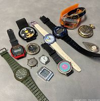 All 11 watches and watch cases displayed on a gray surface, showing various styles and colors including green, black, orange, and metallic.