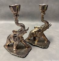 Front view of both elephant candleholders with trunks raised holding candle cups