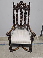 Full view of antique armchair showing carved vertical back panels, crest, and seat upholstery.