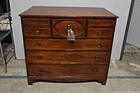 Front view of antique wooden chest with eight drawers and brass hardware, key attached in plastic bag on central drawer handle.