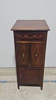 Front view of the antique wooden cabinet showing the drawer and two sets of doors with decorations and keyholes.