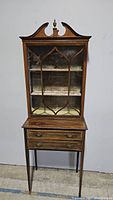 Front view of the antique wooden curio cabinet closed showing two drawers and decorative glass door with muntins.