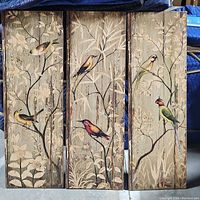 Front view of three wooden art panels with painted birds and floral tree branches