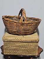 Woven handle basket placed on top of a large wooden basket box with lid.