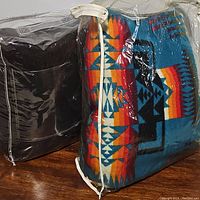 Two blankets packaged in plastic bags showing a brown saddle blanket and a colorful southwestern-patterned blanket.