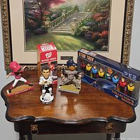 Five collectible figurines displayed on wooden table with painted floral landscape background.