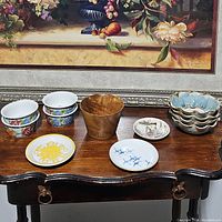 Overview of all decorative bowls and plates on a wooden table with framed artwork behind