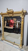 Full view of large ornate gilded mirror standing against wall in warehouse
