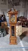 Full view of tall wooden grandfather clock showing overall design and dimensions in a storage environment.