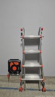 Front view of folded Little Giant ladder with attached black and orange component seen on floor.