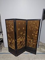 Full view of the three-panel room divider showing embroidered birds and floral designs on brown fabric within dark wooden frames.