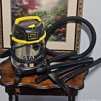 Front view of Stanley wet/dry vacuum cleaner with hose and attachments on a wooden table