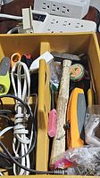 Top view of yellow plastic container with assorted tools including scissors, measuring tape, hammer, utility knife, extension cords, and miscellaneous items.