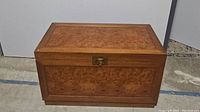 Closed wooden trunk with a brass lock on the front, showcasing a smooth wood grain finish.