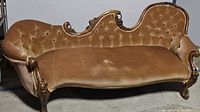 Full front view of Victorian carved wood frame chaise lounge with brown velvet upholstery. Shows the contoured and tufted seat and backrest with wooden curved legs and trim.