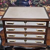 Closed vintage four drawer jewelry box showing brass handles and locks on each drawer.