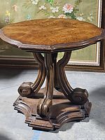 Full view of round wooden pedestal table showing scalloped edges and carved base.