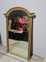 Front view of large arched mirror with ornate gilt frame leaning against wall
