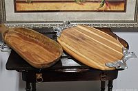 Pair of wooden serving trays on table; one oval with metal fox handles, one rectangular with geometric pattern and metal handle