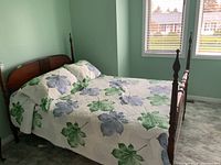 Full view of the four poster wooden bed with floral quilt and mattress in a bedroom with light green walls and carpet.