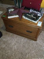 Full view of vintage wooden blanket box with drawer, showing wood grain and metal handles. Two hardcover books, metal star, and metal ring placed on top.
