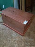 Full side view of the wooden blanket box on carpeted floor showing the rectangular shape and hinged lid.
