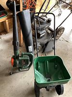 Black and Decker leaf blower and Scotts Turf Builder seeder together in garage setting on concrete floor, showing overall items and condition.